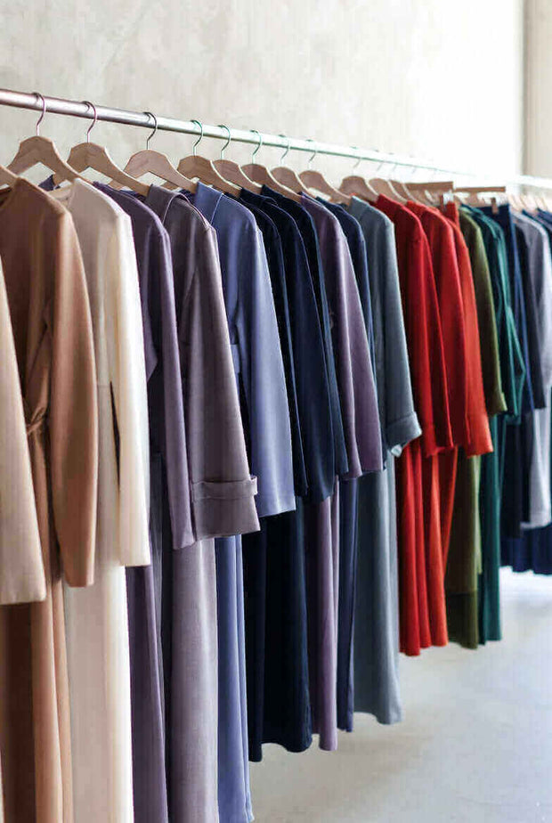 Row of neutral and colorful long-sleeve dresses and tops on wooden hangers in a minimalist boutique rack