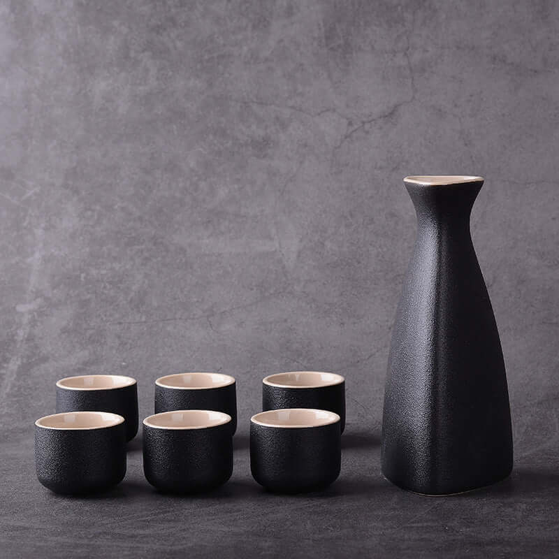 Japanese Ceramic Sake Brewing Ensemble with black sake bottle and six matching cups on a grey background