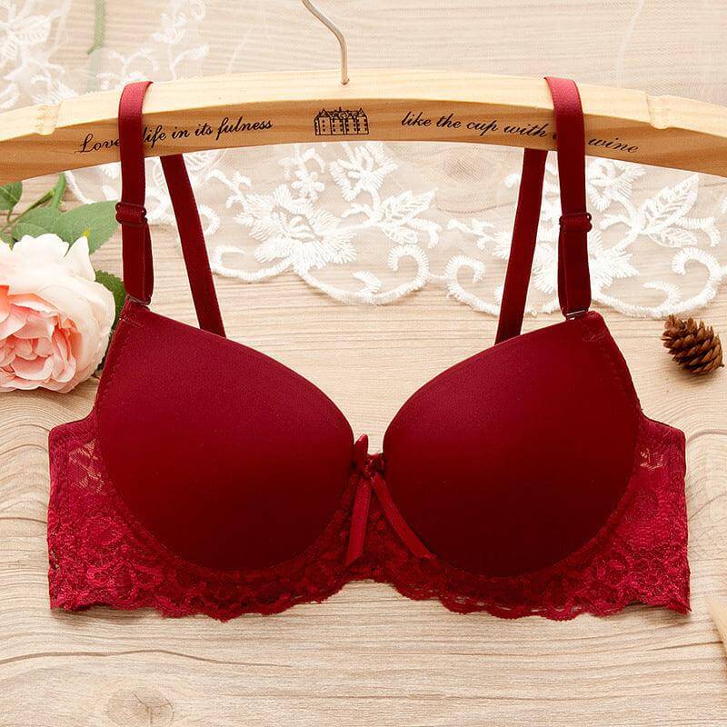 Red underwire gathered bra with lace and bow details for small bust on wooden hanger with floral and lace background.