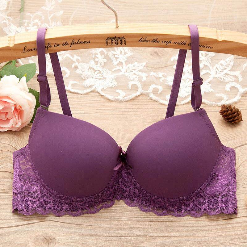 Purple underwire gathered bra with lace and bow details for small bust, displayed on a wooden hanger with flowers in the background