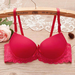 Red underwire gathered bra for small bust with lace and bow details on wooden hanger, next to pink rose and lace fabric.