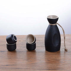 Japanese Ceramic Sake Brewing Ensemble showcasing black sake bottle and cups on a wooden table.