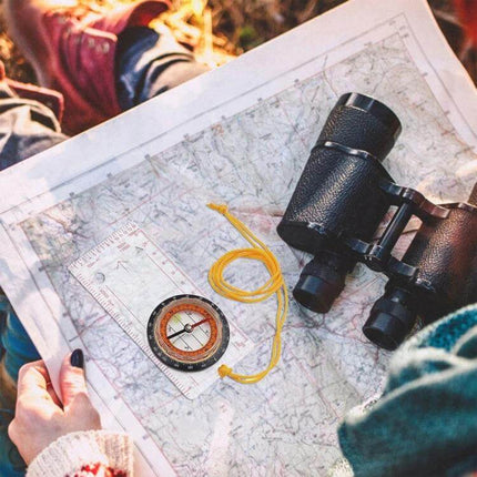 2-In-1 Compass With Map Ruler For Hiking And Outdoors placed on topographic map beside binoculars and map tools for trekking navigation
