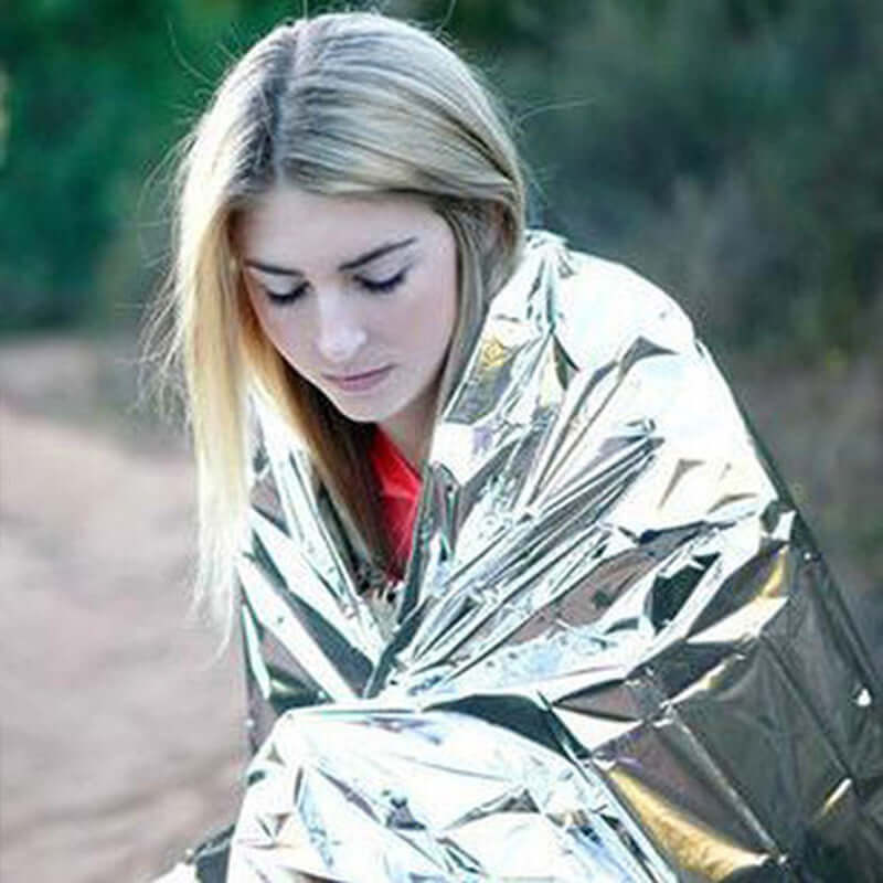 Young woman wrapped in an aluminized emergency blanket for warmth during outdoor survival situation.