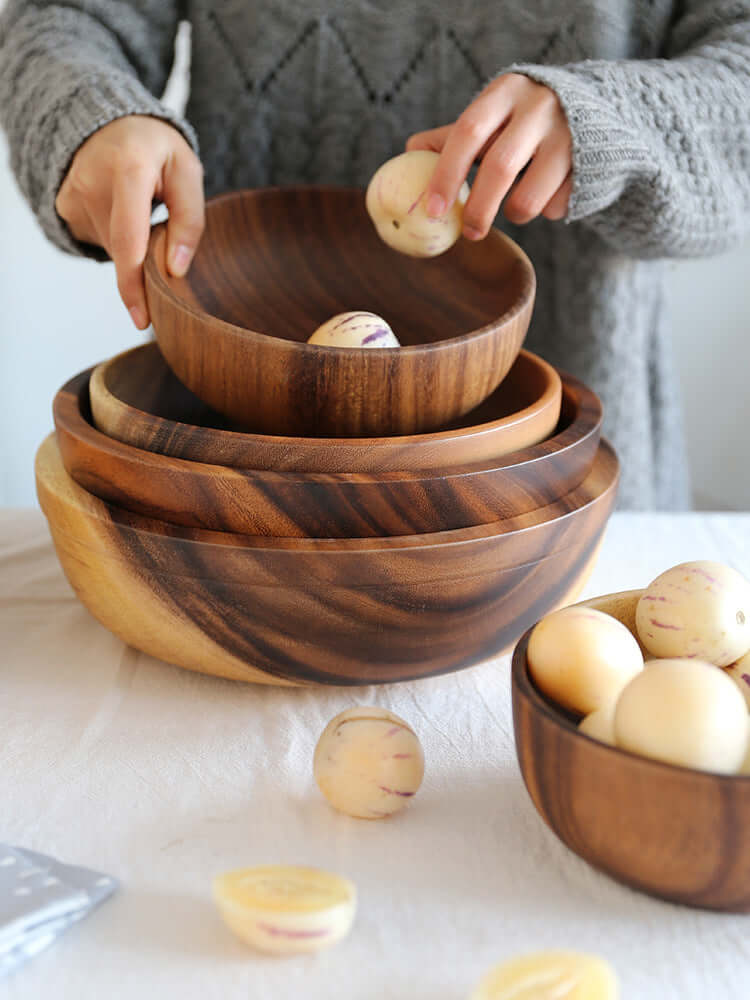 Handcrafted Acacia Wood Bowls on Table with Person Holding Fruits