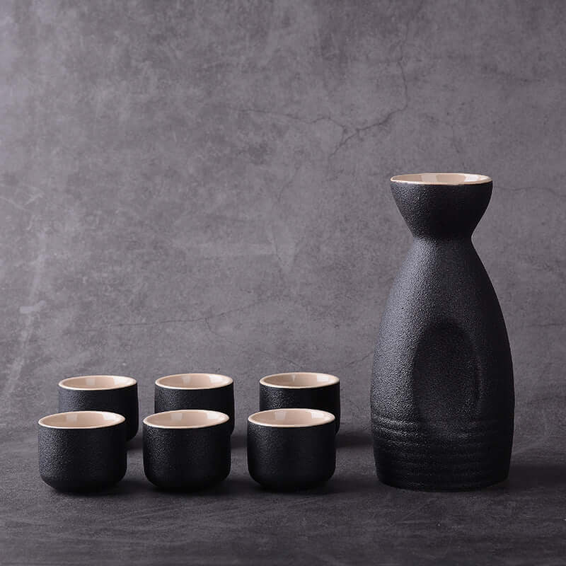 Japanese ceramic sake brewing ensemble with six cups and a carafe against a dark background