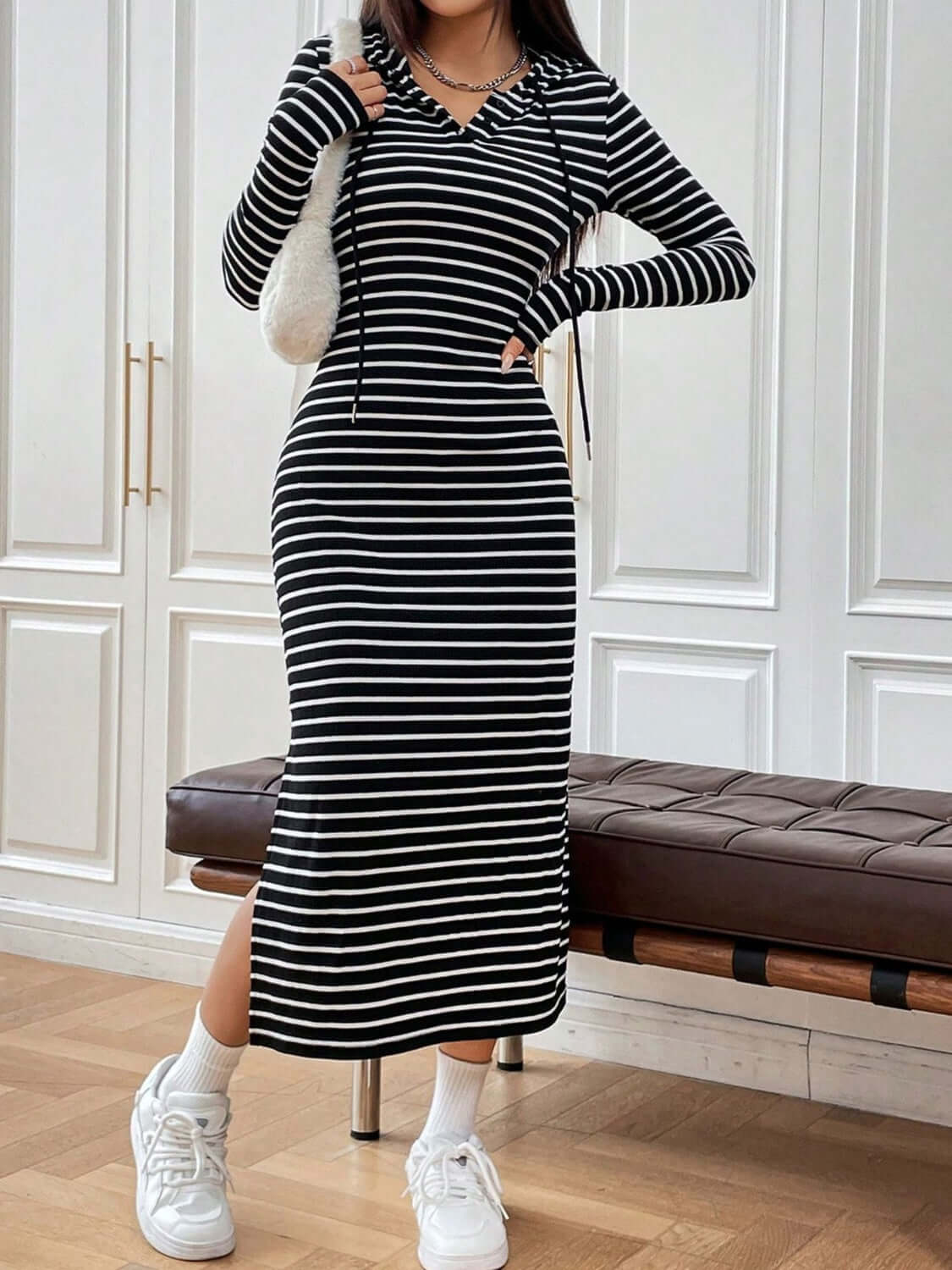 Model wearing a black and white striped long sleeve hooded dress with drawstring, styled casually with sneakers.