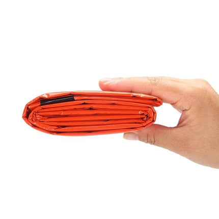 Aotu Orange First Aid Sleeping Bag for Outdoor Camping compact folded emergency blanket in hand, aluminized PE, bright orange visibility