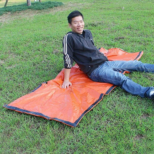 Alt Tag: Aotu Orange First Aid Sleeping Bag for Outdoor Camping laid out on grass with person demonstrating use