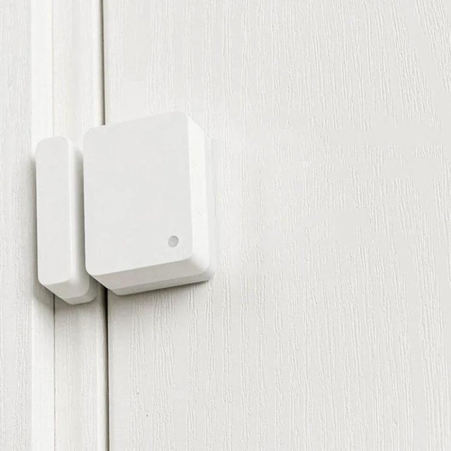 Xiaomi Intelligent Mini Door and Window Sensor for Home Security mounted on white door frame, compact magnetic sensor sending real-time alerts