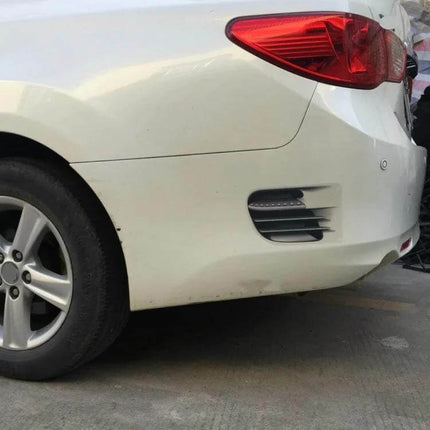 Adhesive Fake Vent Decorative Stickers for Car Surfaces applied to white sedan rear bumper near wheel and taillight