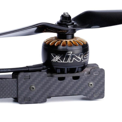 iFlight XING Series Motor for X-Class FPV Racing Drones mounted on carbon fiber arm showing propeller and gold stator accents