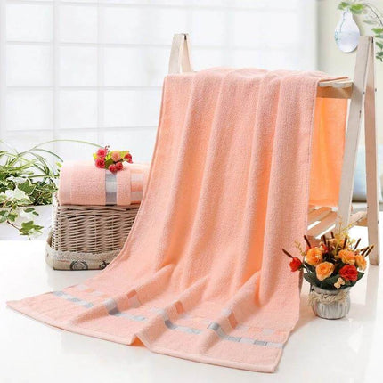 Cotton Plain Bath Towel 140x70 For Daily Bathroom Use - soft peach cotton towel draped with matching rolled towel and flowers