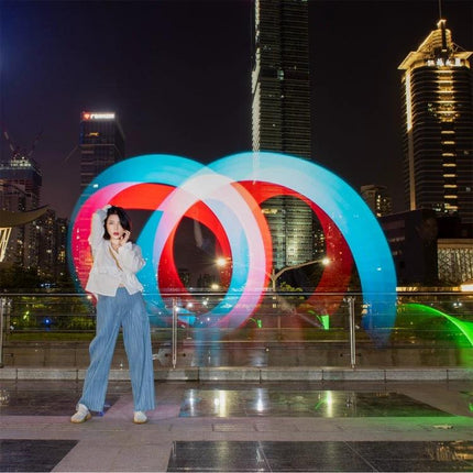 LUXCeO P7RGB Pro Handheld LED Light for Photo and Video Sessions woman posing with colorful long-exposure RGB light trails in urban night scene