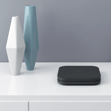 Xiaomi 4K HDR Google TV Streaming Media Player on white shelf next to decorative vases, compact black streaming box for 4K HDR TV