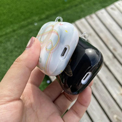Protect Your AirPods During Daily Commutes with IMD Original Case — two decorative IMD cases (white swirl and glossy black) held in hand, charging port visible