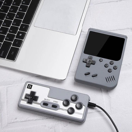 Macaron Mini Handheld Game Console with 800 Built-in Games portable gray handheld and wired controller beside laptop