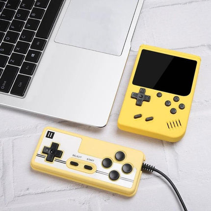 Yellow Macaron Mini Handheld Game Console with 800 Built-in Games next to laptop and wired controller for portable retro play