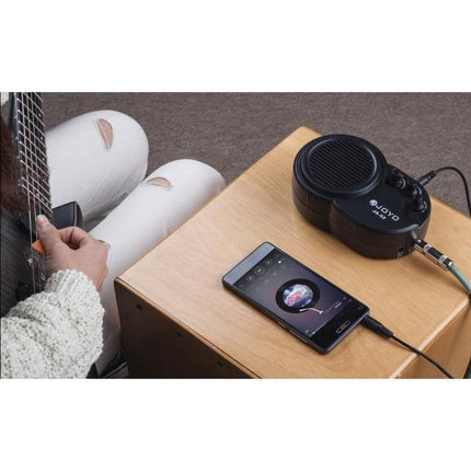 JOYO Mini Guitar Amplifier for Home Practice Sessions on table next to phone and player using electric guitar