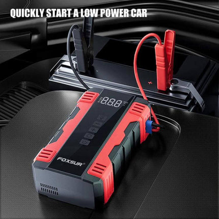 FOXSUR Portable Emergency Car Starter with Air Pump on car seat connected to battery showing digital display and red jumper clamp