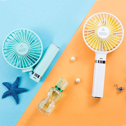 Compact Portable Foldable Handheld Electric Fan with Night Light shown in blue and white on split blue and orange background with perfume bottle and starfish