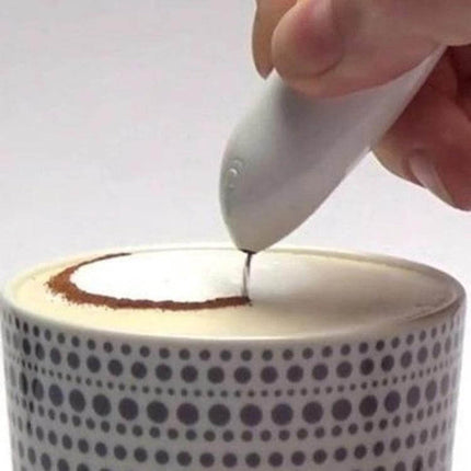 Electric Latte Art Pen for Coffee and Cake Decorating drawing a cocoa ring on frothed milk in a patterned mug