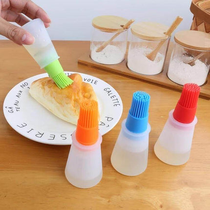 Kitchen Silicone Oil Brush Bottle 70ml being used to brush olive oil on bread with multiple colorful silicone brushes on a wooden counter