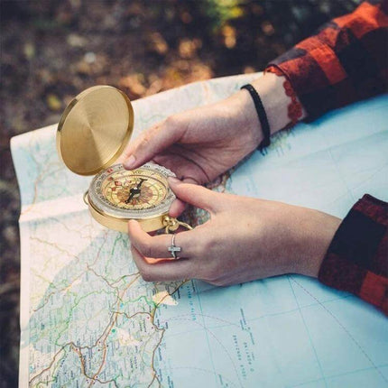 Brass Pocket Compass With Luminous Display For Outdoor Navigation held over a map by a hiker, compact brass and copper shell for night readability