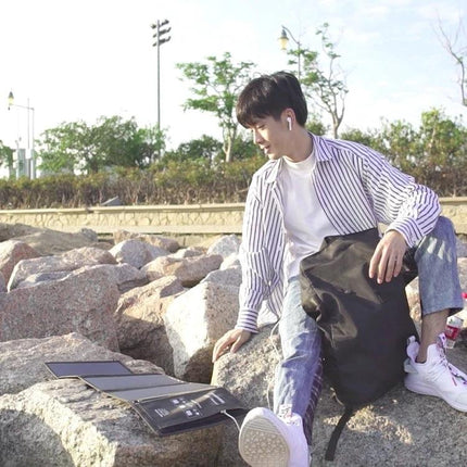 HAWEEL Foldable Solar Charger for On-the-Go Device Powering shown unfolded on rocks charging a tablet outdoors near a hiker
