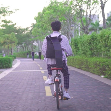 HAWEEL Portable Foldable Solar Charger for Travel and Outdoors attached to backpack while cyclist rides on park path