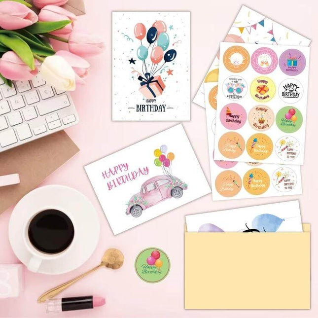 Happy Birthday Greeting Cards 24-Card Set with Envelopes showing folded cards, sticker sheets, envelopes and gift-box packaging on a pink desk