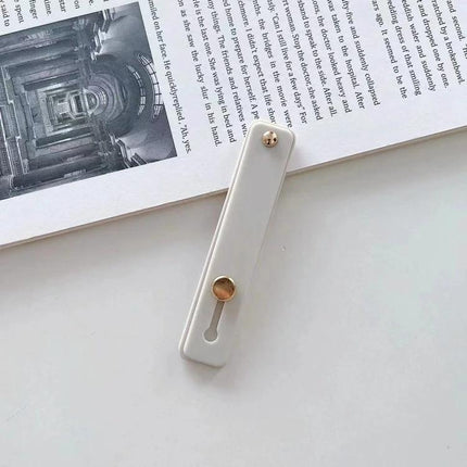 Versatile TPU Leather Phone Finger Strap Holder and Stand white leather strap with gold swivel on book background