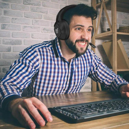 Onikuma Gaming Headset With Adjustable Lightweight Comfort Fit worn by smiling gamer at desk with keyboard and microphone
