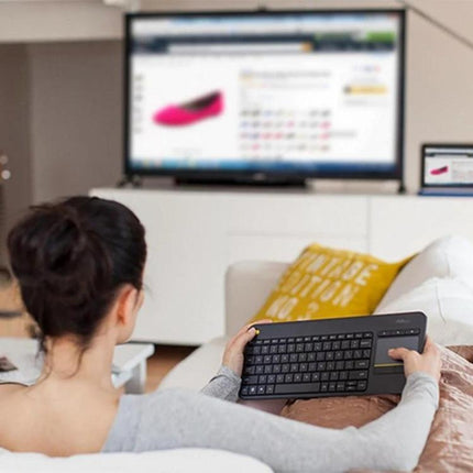 Logitech K400 Plus Wireless Keyboard for Living Room Navigation held by person on couch using built-in touchpad to control TV from 10m range