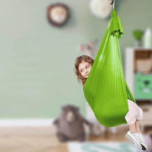 Kids Elastic Hammock Swing 100x280 cm in green fabric with child swinging indoors, sturdy metal hardware and soft stretch satin for playroom lounging