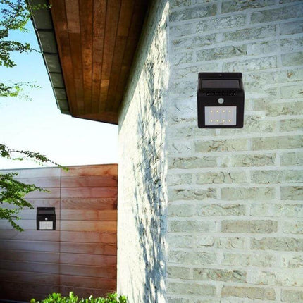 Solar Motion Sensor Wall Light For Outdoors With 8 LEDs mounted on brick exterior illuminating doorway and walkway with solar panel