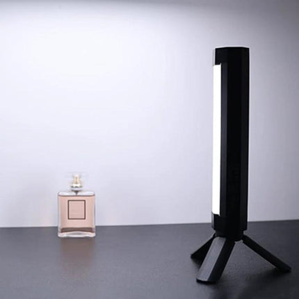 LUXCeO Portable Folding Plastic Tripod for Camera Stability shown supporting a vertical LED light beside a perfume bottle on a tabletop