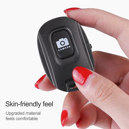 Compact Wireless Bluetooth One-Button Selfie Remote for Smartphones held between fingers showing single camera button and skin-friendly design
