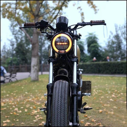 Vintage 5.75 Inch LED Headlight for Harley Motorcycles mounted on classic motorcycle front, illuminated amber halo for improved night visibility
