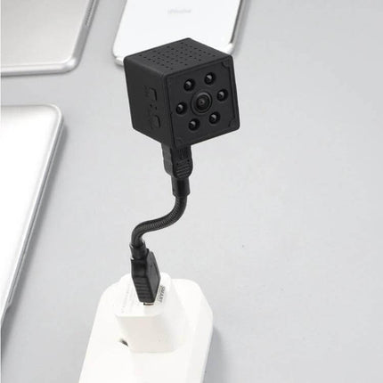 Smart Home WiFi Security Camera with Motion Detection and Night Vision plugged into charger showing compact cube camera, 1080P HD night vision and motion alerts