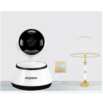 Anpwoo WiFi IP Camera for Home Monitoring with Night Vision placed on a table next to a lamp showing camera lens and power connection