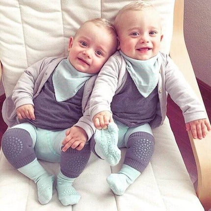 Baby Knee and Elbow Guard Pads for Crawling and Walking Grey on twin babies wearing grey pads and mint outfits, smiling on a chair