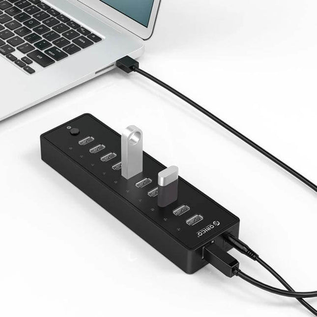 Orico 10-Port USB Hub for Connecting Multiple Devices Black showing multiple USB drives and cables connected to a laptop in a home office setup