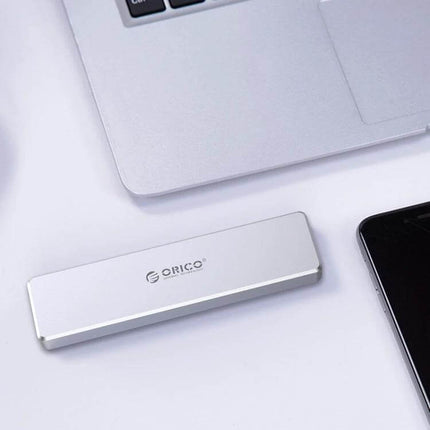 Orico Enclosure for M.2 SSD Storage via USB-C, Up to 2TB Capacity shown next to laptop and phone for portable high-speed storage
