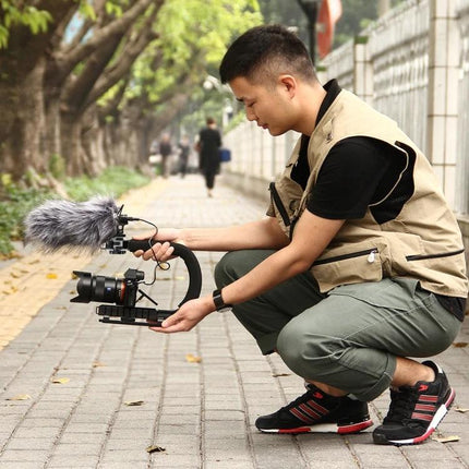 PULUZ C-Shaped Handheld Camera Stabilizer for Video Filming used by videographer crouching on sidewalk to capture smooth low-angle footage