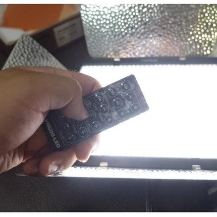 Yongnuo LED Video Light for Canon, Nikon, and Sony DSLR Cameras showing hand holding remote control over illuminated panel to adjust brightness and color temperature