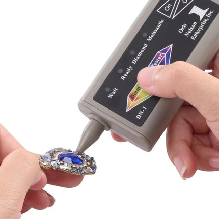 Portable Moissanite and Diamond Tester with US Plug validating a blue gemstone pendant held by hand