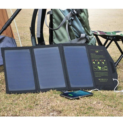 ALLPOWERS Foldable Waterproof Solar Charger for Portability laid out on grass charging a smartphone near a backpack during camping