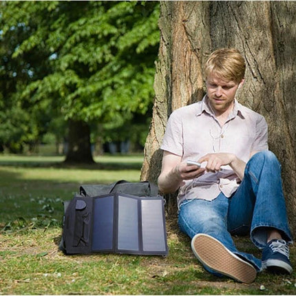 ALLPOWERS Foldable Waterproof Solar Charger for Portability powering a smartphone outdoors while a man sits against a tree