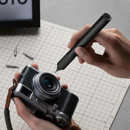 Xiaomi Mijia 25-in-1 Rechargeable Precision Screwdriver for Repairs held above a compact camera showing magnetic bit and precision repair use